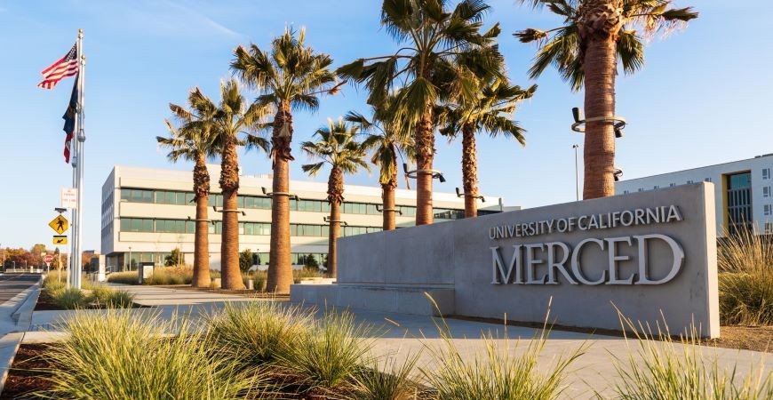UC Merced Sign with palm trees and the admin building in the background